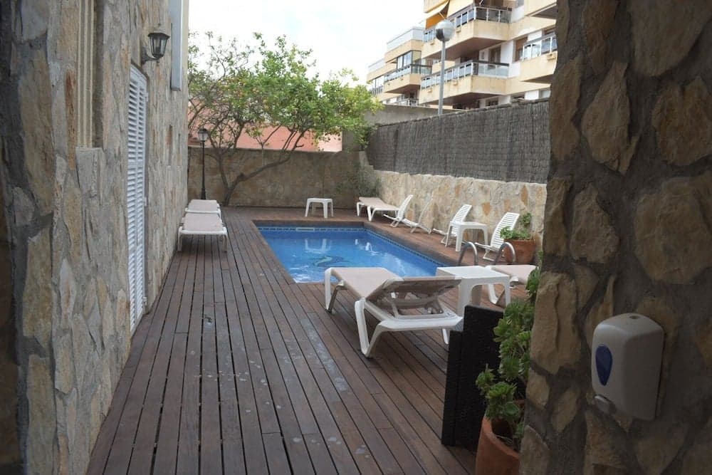 A serene private pool deck surrounded by stone walls and wooden flooring offers a cozy retreat with lounge chairs, tables, and lush greenery, ideal for a relaxing vacation getaway.