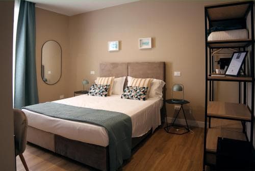 A cozy hotel room features a neatly made bed with patterned pillows, modern bedside tables, and a stylish shelving unit, creating a welcoming atmosphere ideal for travelers seeking comfort and style.