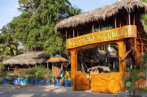 A vibrant tropical hostel entrance with colorful umbrellas and lush greenery invites travelers seeking a relaxed and adventurous getaway in a serene outdoor setting.