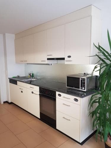 A modern, minimalist kitchen with sleek white cabinets, black countertops, and stainless steel appliances creates a clean and functional space ideal for travelers seeking self-catering accommodations.