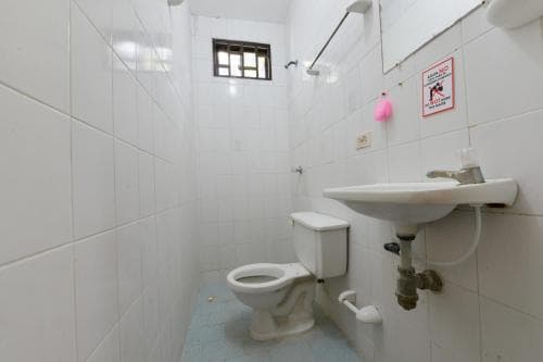 A compact, functional bathroom with white tiled walls, a toilet, sink, and small window offers a practical space for travelers seeking basic amenities in budget accommodations.