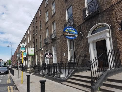 A charming urban street scene featuring a brick building with a hostel entrance, arched doorway, and colorful signage, evoking a welcoming and historic atmosphere ideal for budget travelers exploring the city.