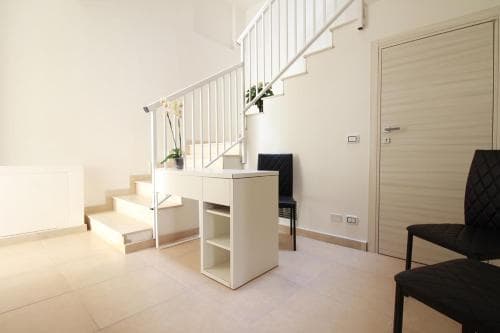 A minimalist apartment interior features a sleek white staircase, modern furniture, and a clean aesthetic, ideal for travelers seeking a cozy and stylish urban retreat.
