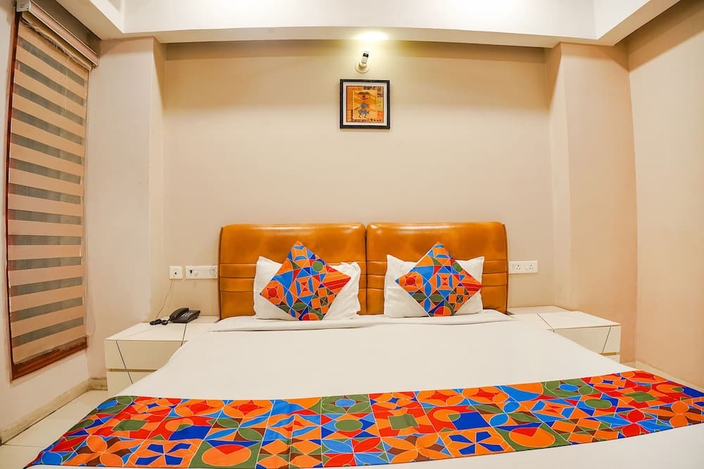A cozy hotel room features a vibrant bedspread and pillows against a minimalist beige backdrop, ideal for travelers seeking comfort and a touch of color in their accommodations.
