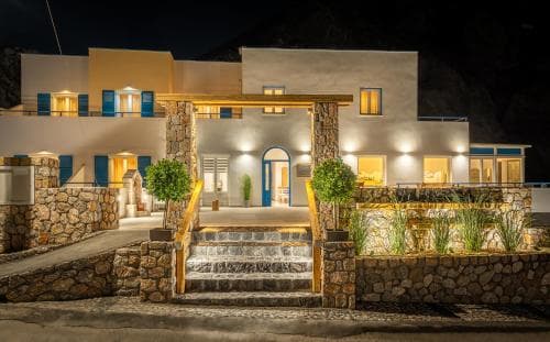 A warmly lit Mediterranean-style villa at night, featuring stone steps, potted plants, and glowing windows, creates an inviting atmosphere ideal for travelers seeking a cozy retreat.