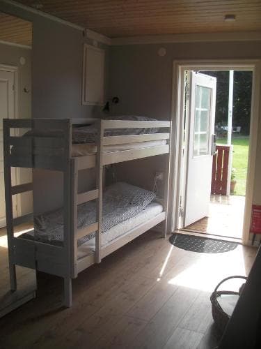 A cozy cabin bedroom with bunk beds bathed in natural light from an open door leading to a serene grassy outdoor space, ideal for family retreats or nature escapes.