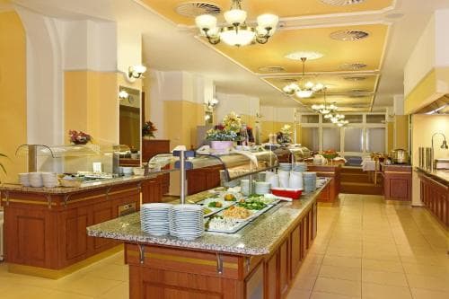 A warmly lit hotel buffet area features an inviting spread of food on polished wooden counters, adorned with floral arrangements and elegant chandeliers, perfect for travelers seeking a comfortable dining experience.