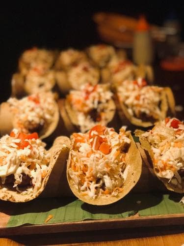 A vibrant display of colorful tacos filled with shredded vegetables and garnished with fresh toppings sits invitingly on a wooden tray, perfect for a lively street food adventure or casual dining experience.