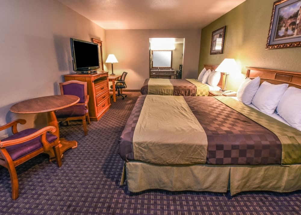 A cozy hotel room features two neatly made beds, a warm-toned color scheme, a small dining area, and a television, ideal for travelers seeking comfort and convenience during their stay.