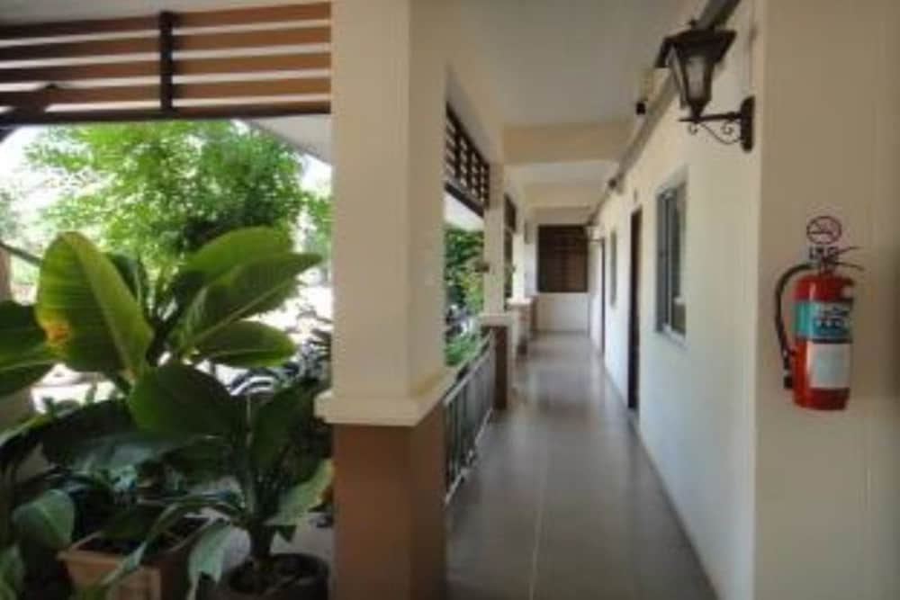 A serene hotel corridor lined with lush greenery and a mounted fire extinguisher offers travelers a tranquil and safe accommodation experience.
