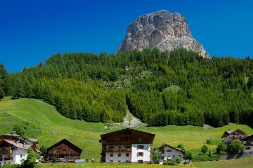 A serene mountain village with quaint houses nestled among lush green hills under a clear blue sky, ideal for tranquil alpine retreats and nature photography.