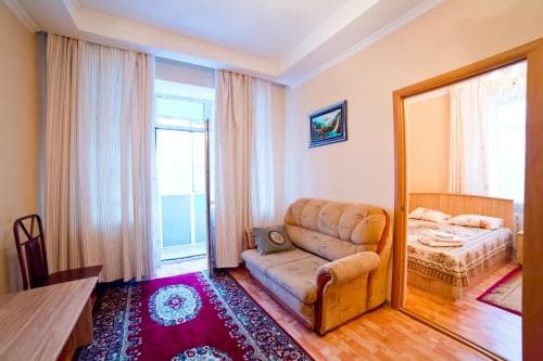 A cozy hotel room features a plush sofa, vibrant rug, and mirrored reflection of a neatly made bed, creating an inviting atmosphere ideal for travelers seeking comfort and relaxation.
