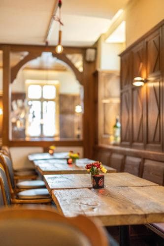 A cozy restaurant interior features rustic wooden tables adorned with vibrant flower vases, warm lighting, and arched doorways, creating an inviting atmosphere perfect for travelers seeking a charming dining experience.