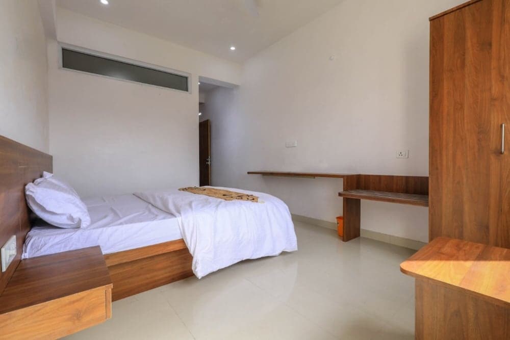 A minimalist hotel room features a neatly made bed, wooden furniture, and a clean white aesthetic, ideal for travelers seeking simplicity and comfort.
