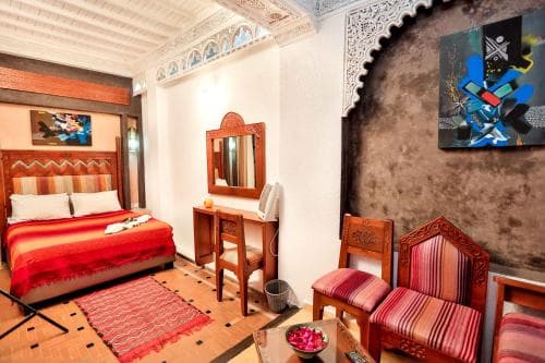 A cozy, ornately decorated room with vibrant red accents, traditional Moroccan furniture, and artistic wall hangings offers a serene retreat for travelers seeking cultural immersion in a boutique hotel setting.