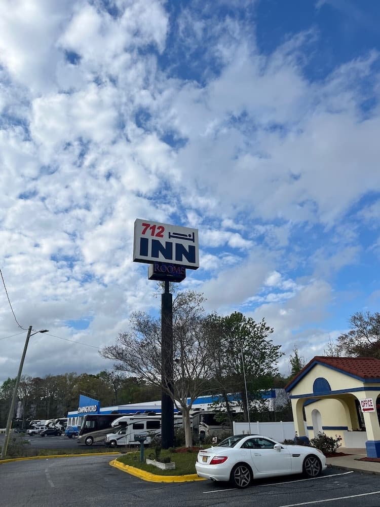 A serene roadside scene features the "712 Inn" sign under a partly cloudy sky, with parked RVs and a white convertible car enhancing its welcoming atmosphere for travelers seeking accommodation.