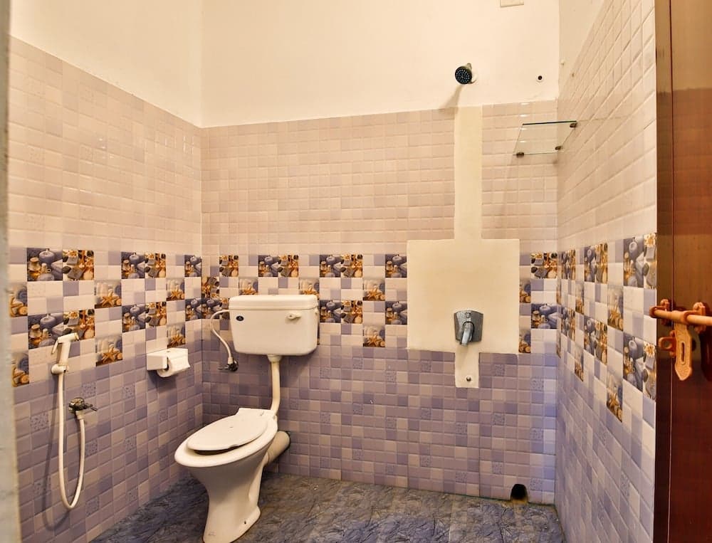 A cozy bathroom with purple mosaic tiles, a toilet, bidet spray, and a mounted showerhead offers a functional and inviting space for travelers seeking comfort during their stay.