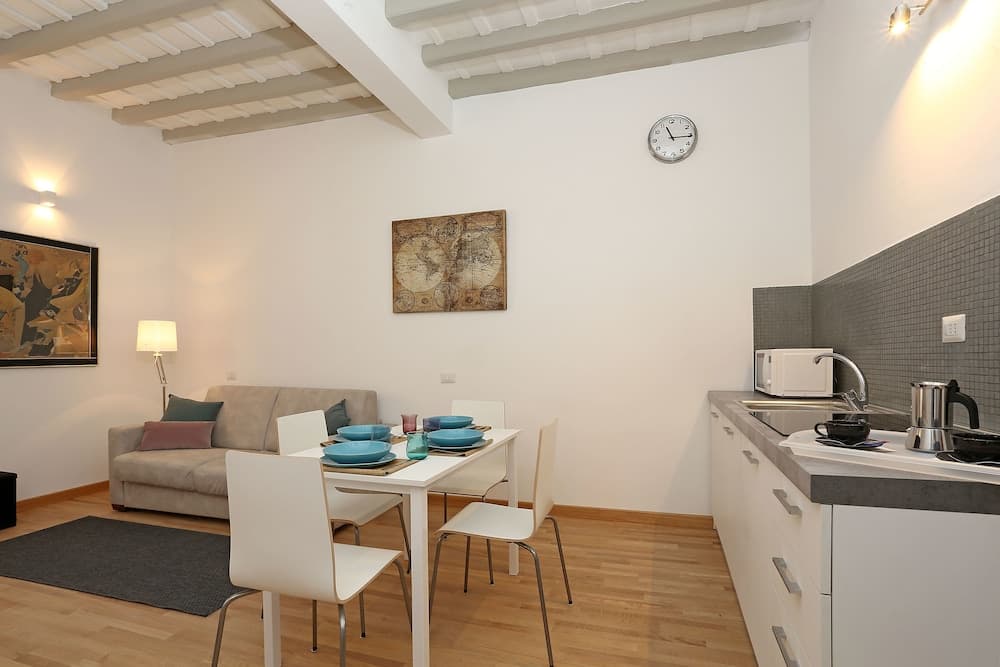 A cozy studio apartment with exposed wooden beams, a modern kitchenette, and a dining area set for four, ideal for travelers seeking a comfortable and stylish urban retreat.