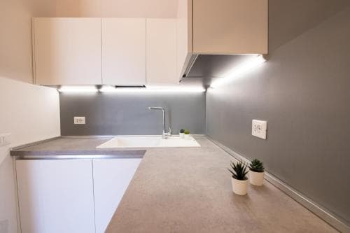 A sleek, modern kitchen with minimalist white cabinets, stainless steel countertops, and small potted plants creates a clean and inviting atmosphere, ideal for travelers seeking a cozy self-catering accommodation.