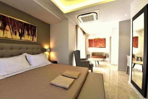 A cozy hotel suite features a neatly made bed, modern furnishings, warm lighting, and vibrant artwork, creating an inviting atmosphere ideal for travelers seeking comfort and style during their stay.