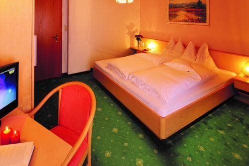 A cozy hotel room with warm lighting, a neatly made bed, a red armchair, and a small TV, evokes a relaxing atmosphere ideal for travelers seeking comfort and tranquility.