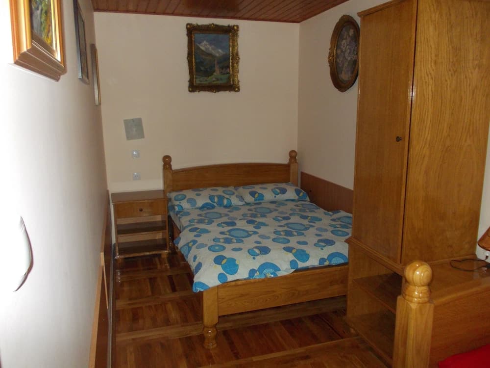 A cozy bedroom with wooden furnishings, a blue-patterned bedspread, framed artwork on white walls, and warm lighting creates an inviting atmosphere ideal for travelers seeking comfort in a rustic retreat.