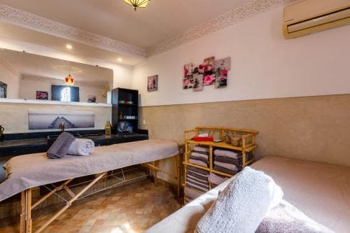 A serene massage therapy room features wooden tables draped in white linens, neatly folded towels on a wooden rack, and calming decor, ideal for travelers seeking relaxation and wellness services.