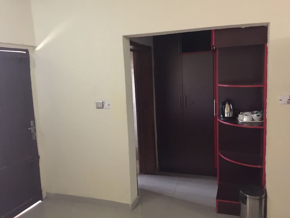 A cozy hotel room hallway features a dark wooden wardrobe, red shelving with tea-making essentials, and a sleek trash bin, ideal for travelers seeking comfort and convenience.