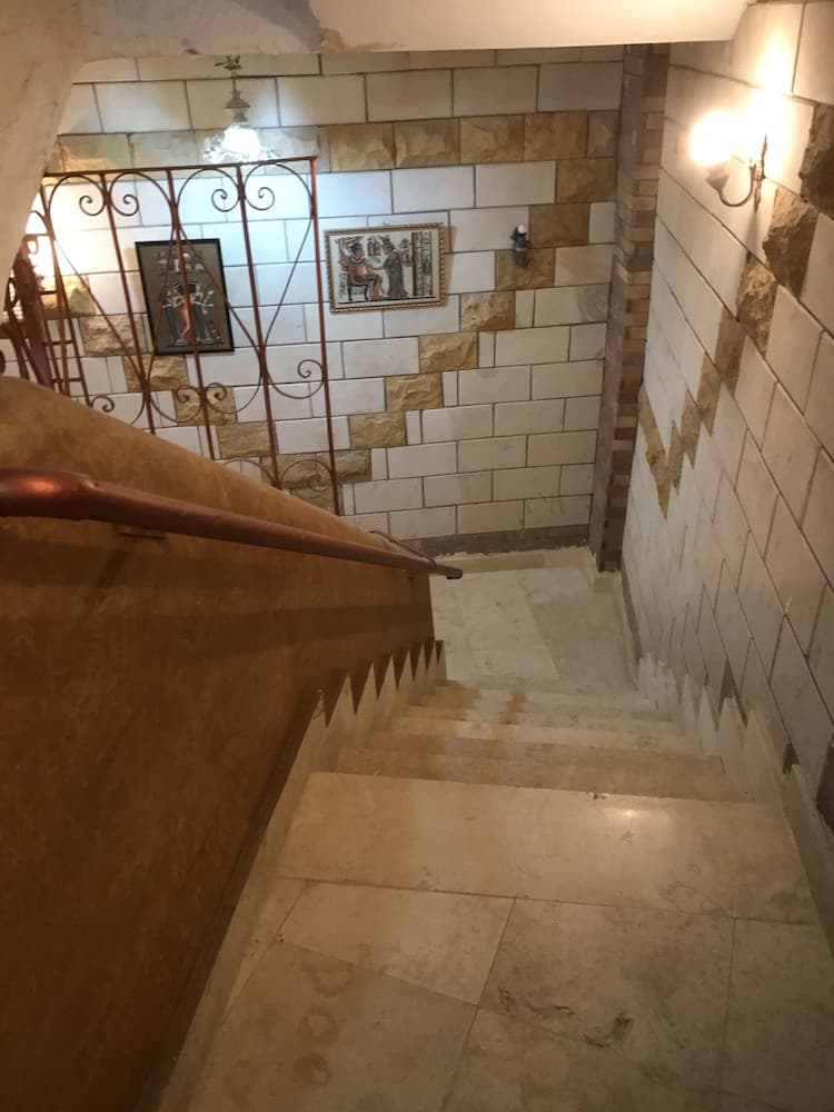A warmly lit stone staircase adorned with framed artwork and intricate metal railings creates an inviting atmosphere for travelers exploring historic indoor settings.