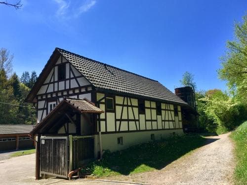 A serene rural scene featuring a traditional half-timbered house under a clear blue sky, surrounded by lush greenery, ideal for countryside retreats and cultural exploration.