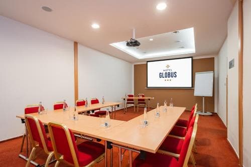 A modern conference room with red chairs, wooden tables, and a large screen displaying "GLOBUS" offers an ideal setting for professional meetings and presentations.