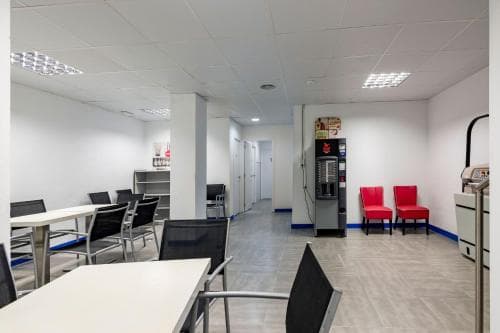 A modern, clean waiting area with white tables, black chairs, vending machines, and red seating offers a comfortable space for travelers to relax in an airport or transit hub.