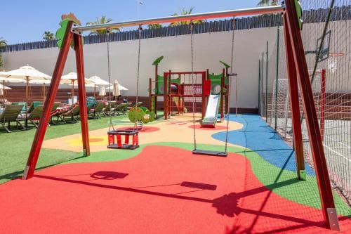 A vibrant playground with colorful swings, slides, and a basketball hoop set against a sunny backdrop, ideal for family-friendly resorts seeking an engaging kids' area.