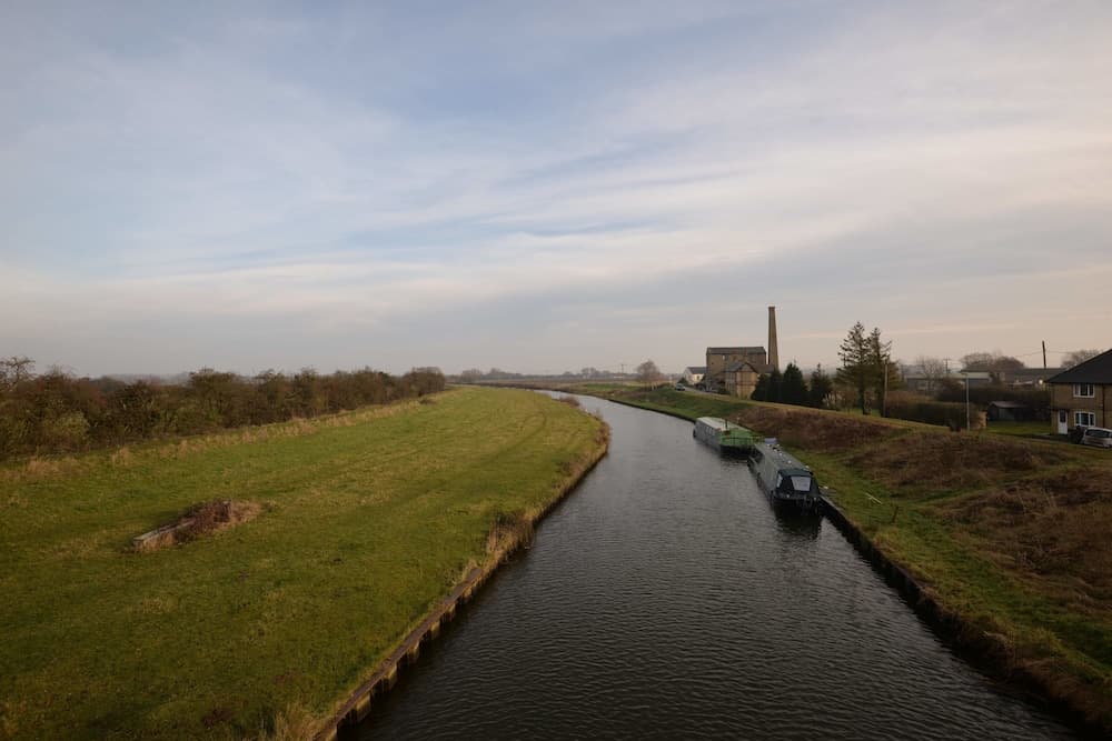 A serene canal scene unfolds with narrowboats docked along grassy banks under a soft sky, ideal for tranquil boating and countryside exploration.