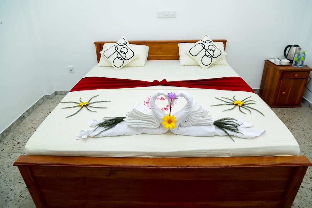 A cozy hotel room features a neatly made bed adorned with towel swans and flowers, creating a welcoming and romantic atmosphere ideal for travelers seeking comfort and charm.