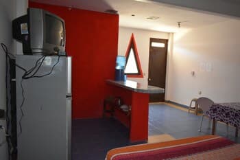 A cozy budget hotel room features vibrant red walls, a small kitchenette, and basic furnishings, creating a welcoming atmosphere ideal for travelers seeking affordable accommodations.