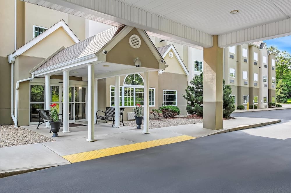 A serene hotel entrance features a covered porch with white columns, comfortable seating, and lush greenery, inviting travelers to relax in a welcoming atmosphere ideal for family vacations or business trips.