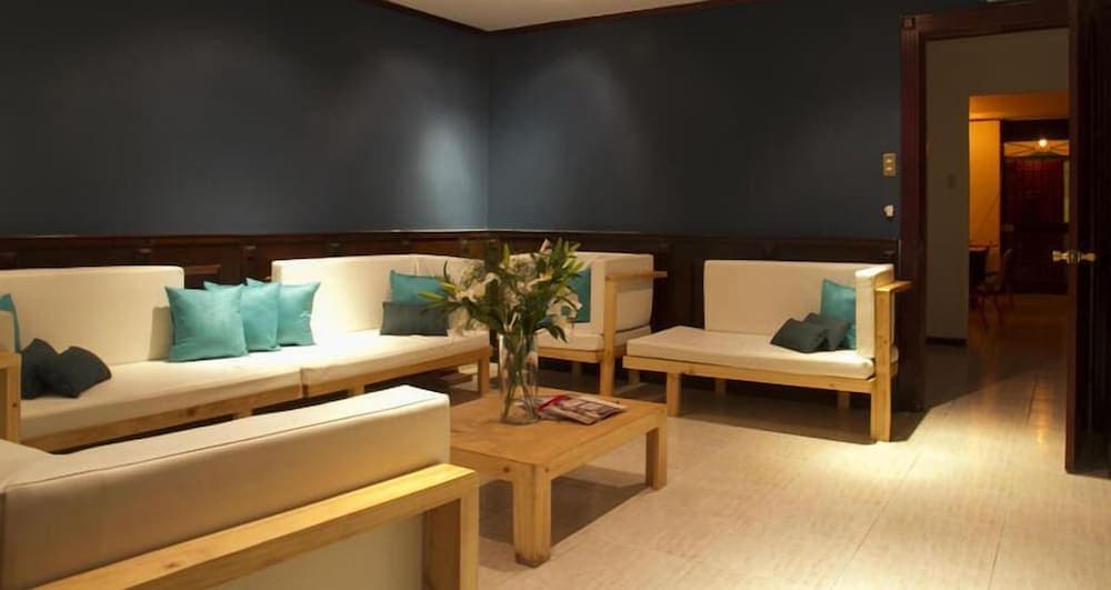 A cozy hotel lounge features modern wooden sofas adorned with teal cushions, a central coffee table with fresh flowers, and warm lighting, creating an inviting atmosphere ideal for travelers seeking relaxation.