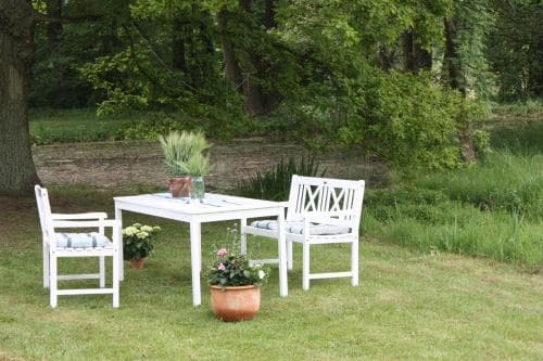 A serene outdoor garden setting features white wooden furniture surrounded by lush greenery, ideal for a peaceful retreat or leisurely picnic.