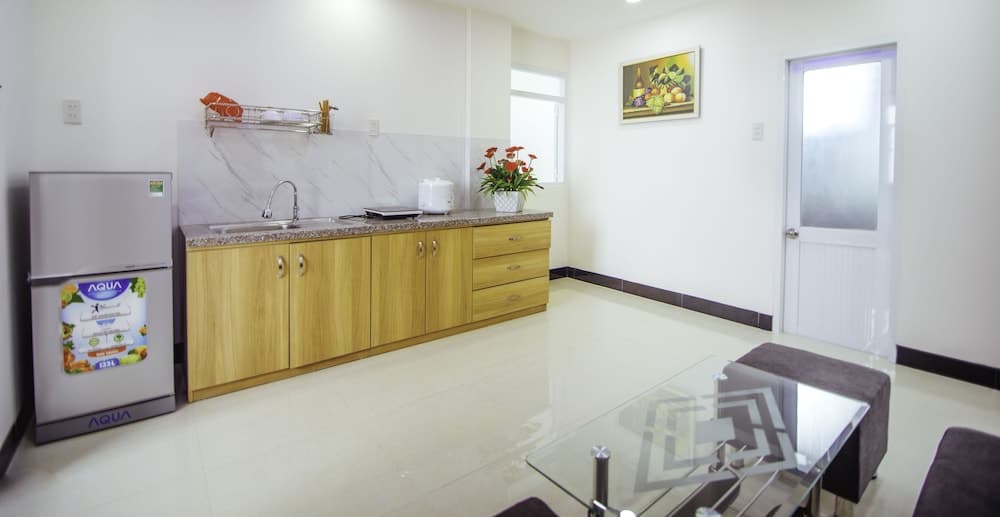 A bright, modern kitchenette with wooden cabinets, a sleek glass-top table, and vibrant flower decor creates an inviting atmosphere ideal for travelers seeking a cozy apartment stay.