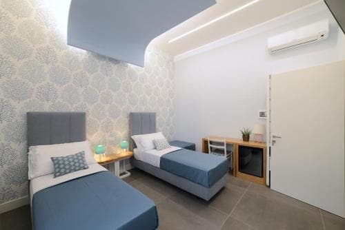 A cozy modern bedroom with two single beds, patterned wallpaper, and minimalist decor offers a serene retreat for travelers seeking comfort in a boutique hotel setting.