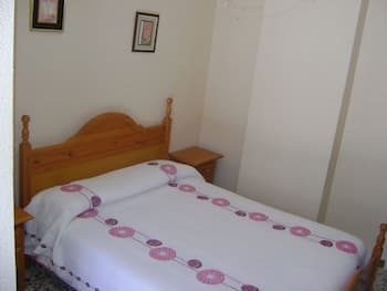 A cozy bedroom with a neatly made bed adorned in purple floral bedding, framed by wooden furniture and simple decor, evokes a serene and inviting atmosphere ideal for travelers seeking a peaceful retreat.