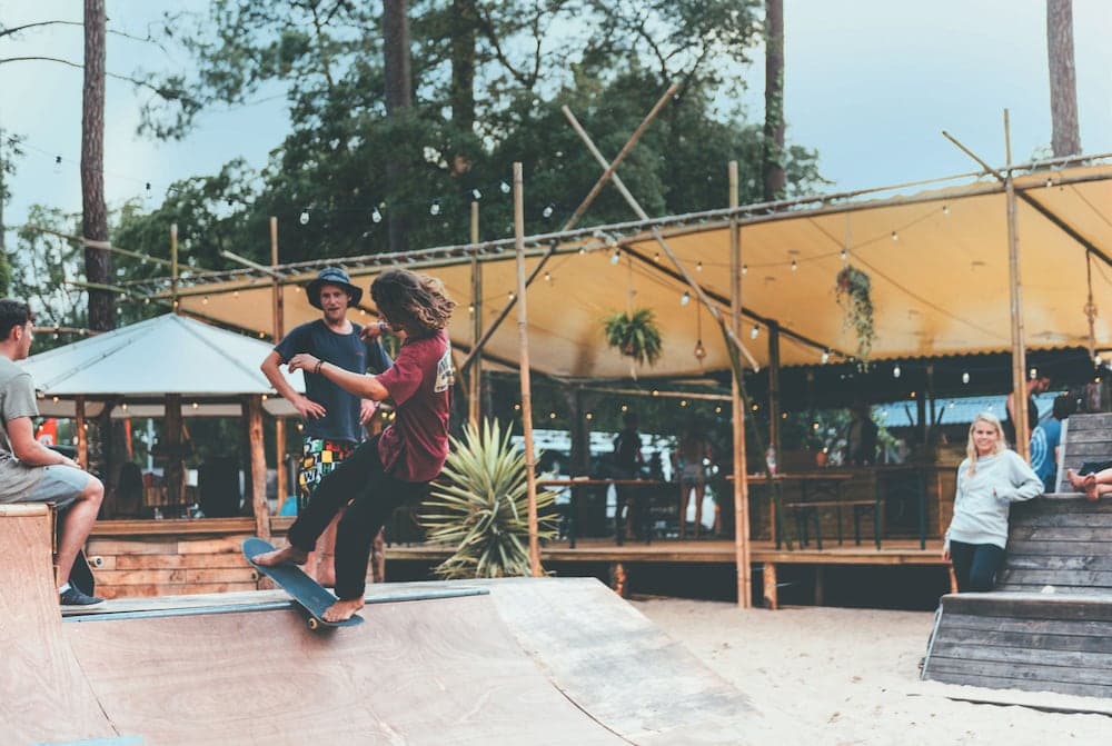 A lively outdoor skate park under a canopy of string lights and trees offers an adventurous atmosphere with ramps, wooden structures, and a relaxed gathering spot for travelers seeking active and social experiences.
