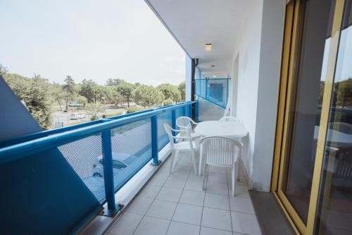 A serene hotel balcony with blue railings overlooks lush greenery, featuring white plastic chairs and tables, ideal for travelers seeking relaxation and a peaceful retreat.