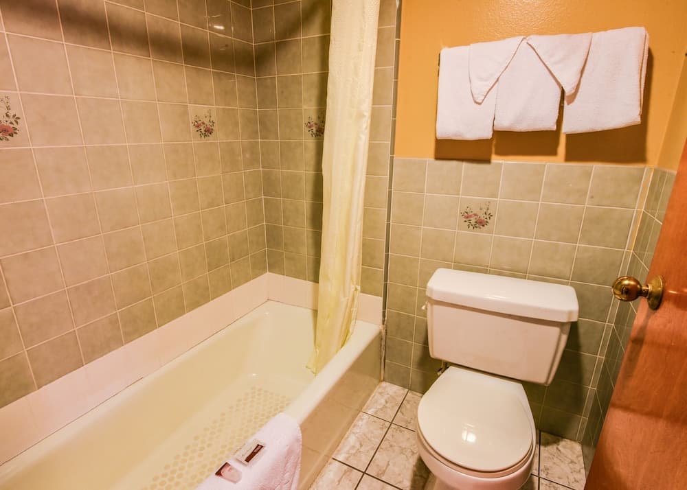 A cozy bathroom with floral-tiled walls, a bathtub, toilet, neatly folded towels on a rack, and a warm ambiance ideal for travelers seeking comfort and cleanliness.