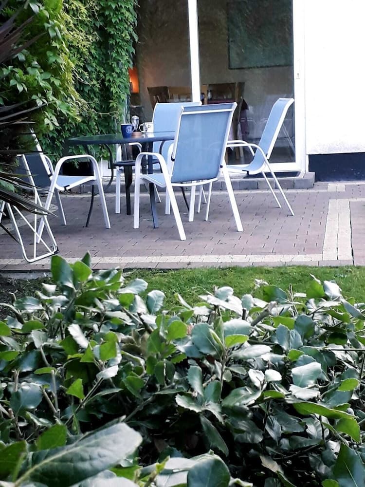 A serene outdoor patio with modern chairs and a table surrounded by lush greenery invites travelers to relax and enjoy a peaceful retreat.