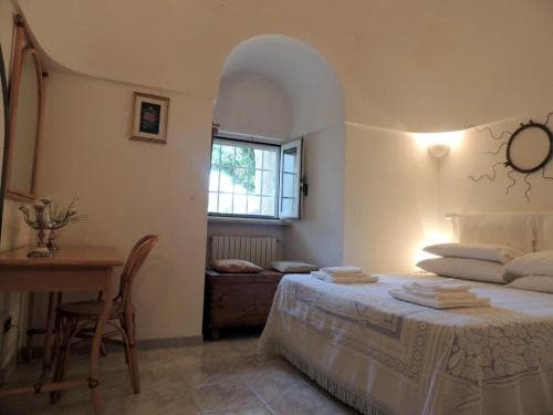 A cozy Mediterranean-style bedroom with arched ceilings, a wooden desk, and a neatly made bed bathed in soft natural light from an open window, ideal for travelers seeking a serene and charming accommodation experience.