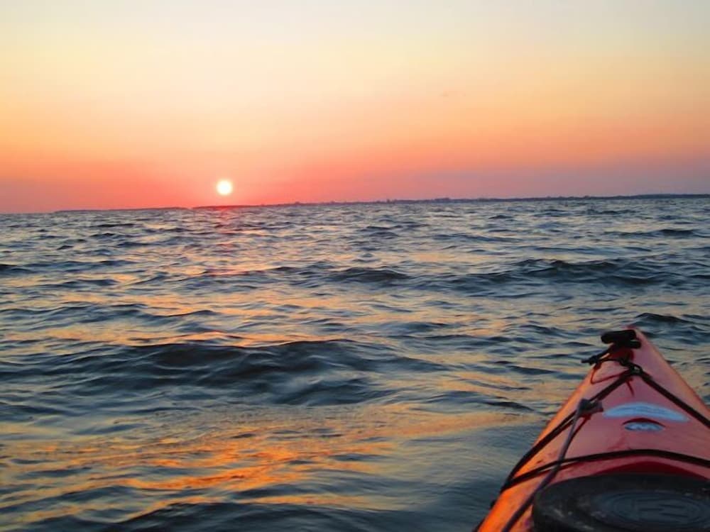 A serene sunset over the ocean viewed from a kayak creates a tranquil mood, perfect for adventure seekers looking to experience nature's beauty up close.