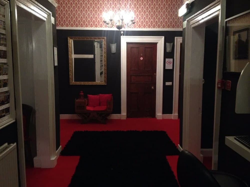A cozy hotel lobby features vibrant red carpeting, a plush red bench, ornate wallpaper, and a chandelier, creating an inviting atmosphere ideal for travelers seeking comfort and charm.
