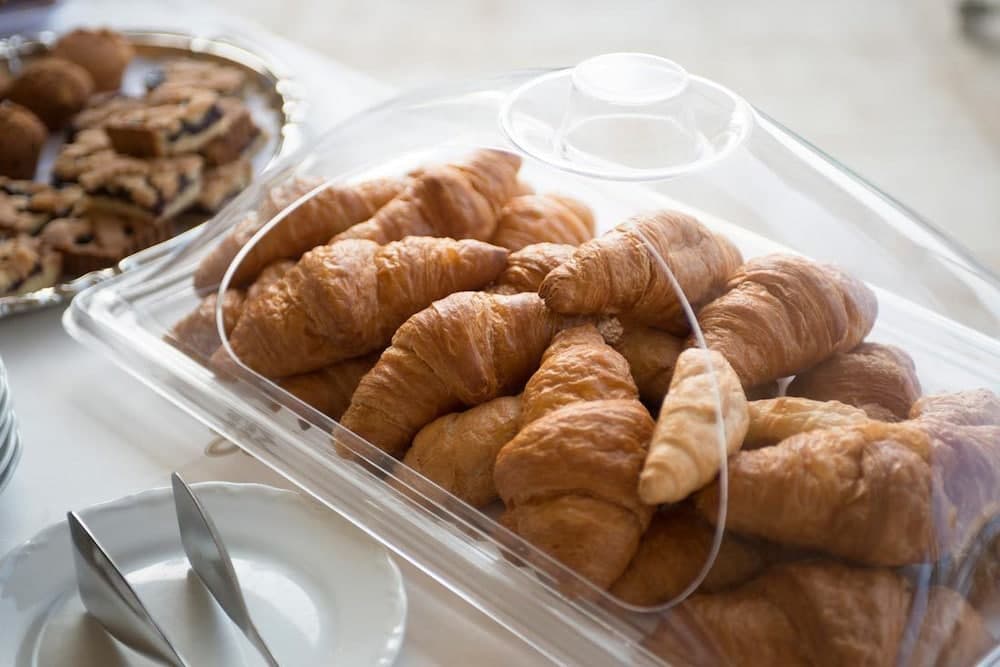 A cozy breakfast setting features a clear container filled with golden croissants alongside assorted pastries on a table, ideal for travelers seeking a delightful morning meal experience.